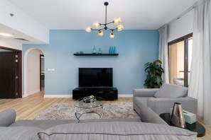 A modern living room with a flat-screen TV, a glass coffee table, and a grey sofa.