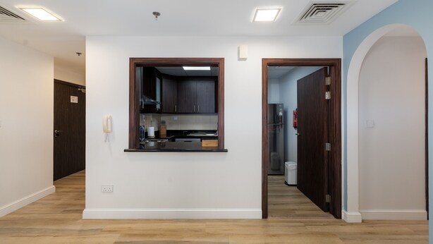 Ein geräumiger Flur mit Holzboden, ein Küchenbereich mit dunklen Schränken und eine Tür zu einem weiteren Zimmer.