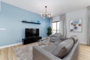 A modern living room with a large flat-screen TV, a grey sofa, a glass coffee table, and a blue accent wall. - Modern JBR 2BR w/ Pool and Gym, Marina Views (Dubai)