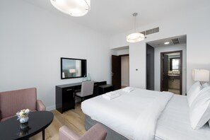 A modern hotel room with a large bed, a desk with a chair, a small table with a vase, and a mirror on the wall.