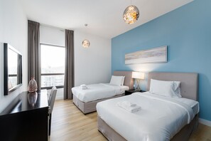 A hotel room with two beds, a desk, and a large window.