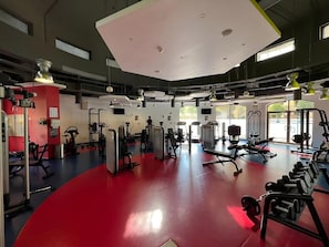 Ein Fitnessstudio mit unterschiedlichen Trainingsgeräten, großen Fenstern und einem roten Boden.