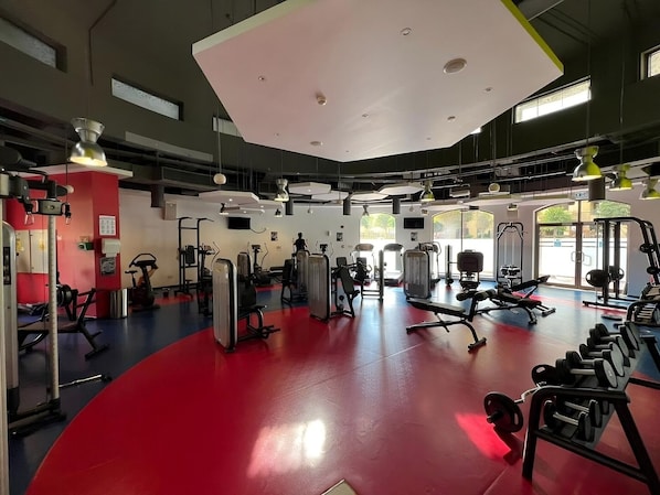 A gym with various exercise equipment, large windows, and a red floor.