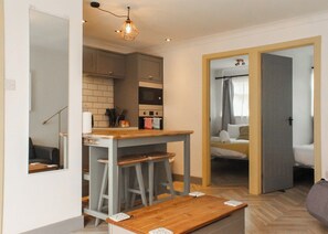 A compact living space with a kitchenette, a dining area with stools, and a bedroom with a bed and curtains.