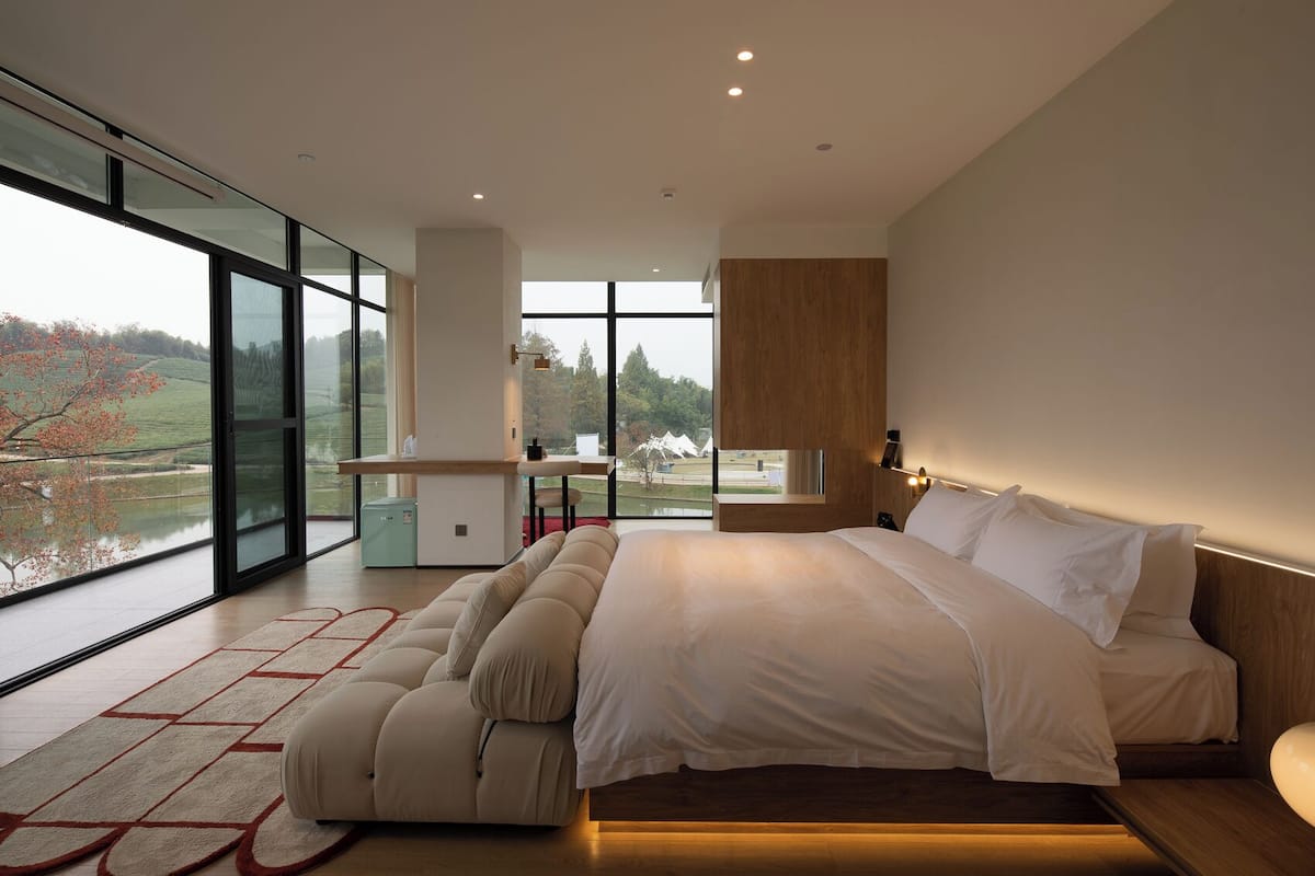 A modern bedroom with a large bed, a desk, and a view of a lake.