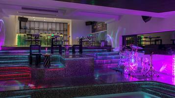 A bar area with a DJ booth, a drum set, and a staircase with illuminated steps.