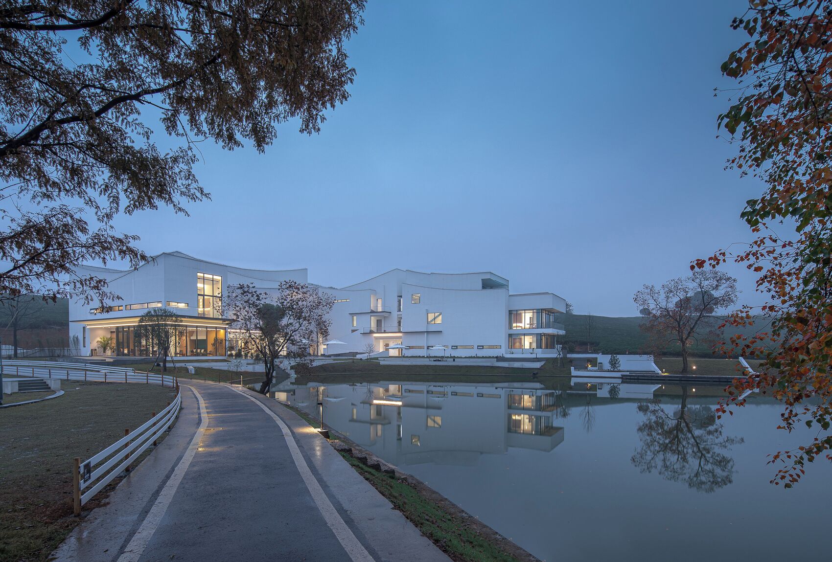 A modern building with large windows and a reflection in a calm body of water.