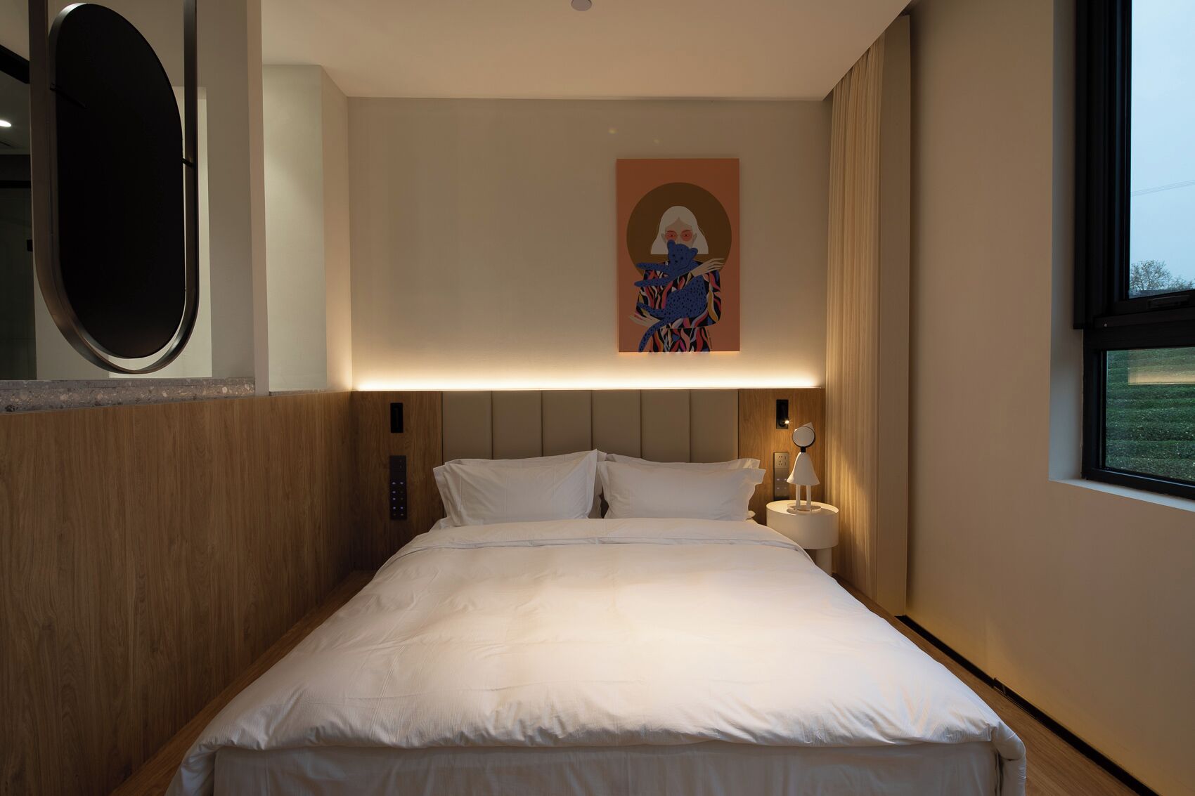 Una habitación de hotel con una cama grande, una obra de arte en la pared, una lámpara de noche y una ventana con vistas.