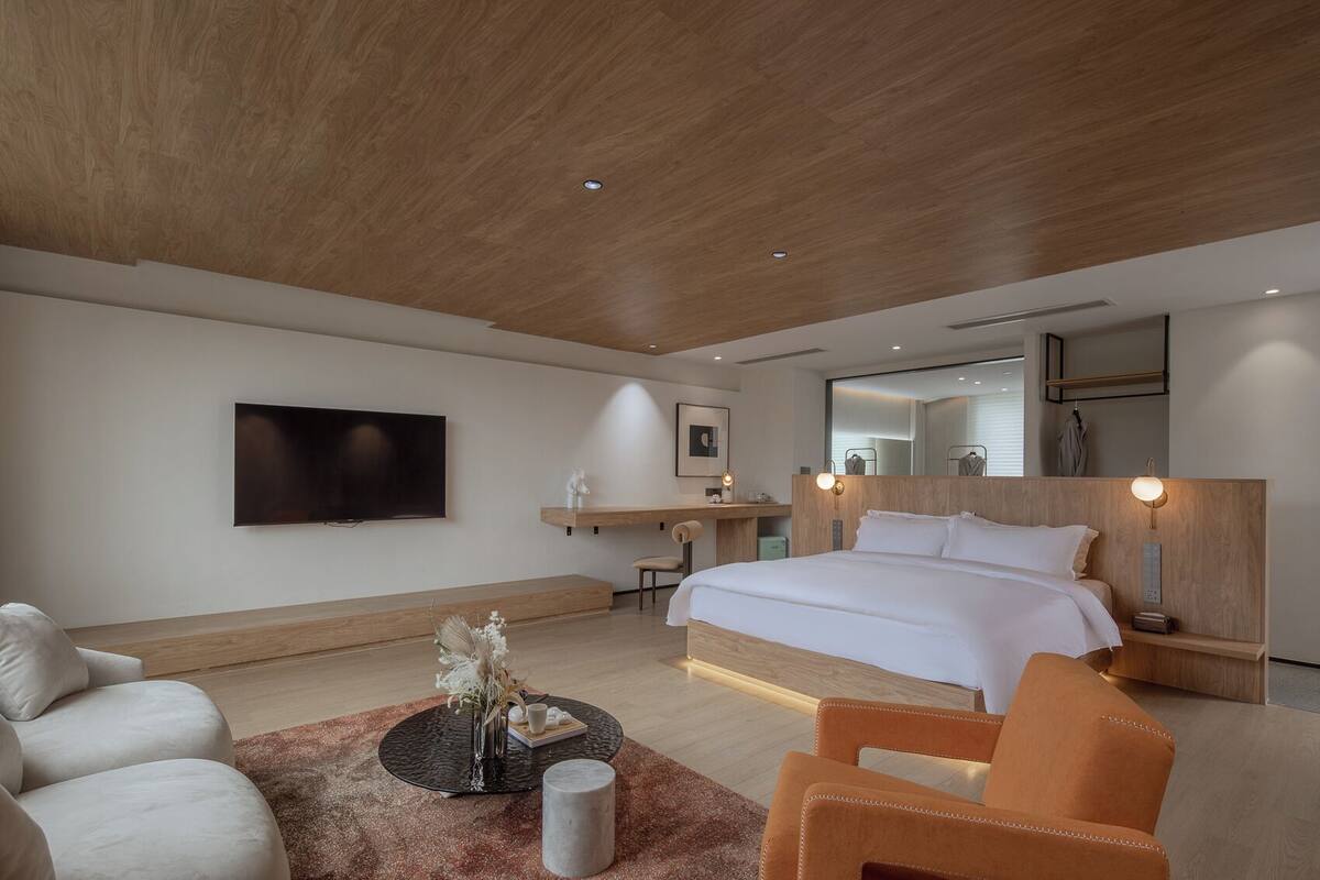 A modern hotel room with a large bed, a flat-screen TV, a desk, and a seating area with a coffee table and chairs.