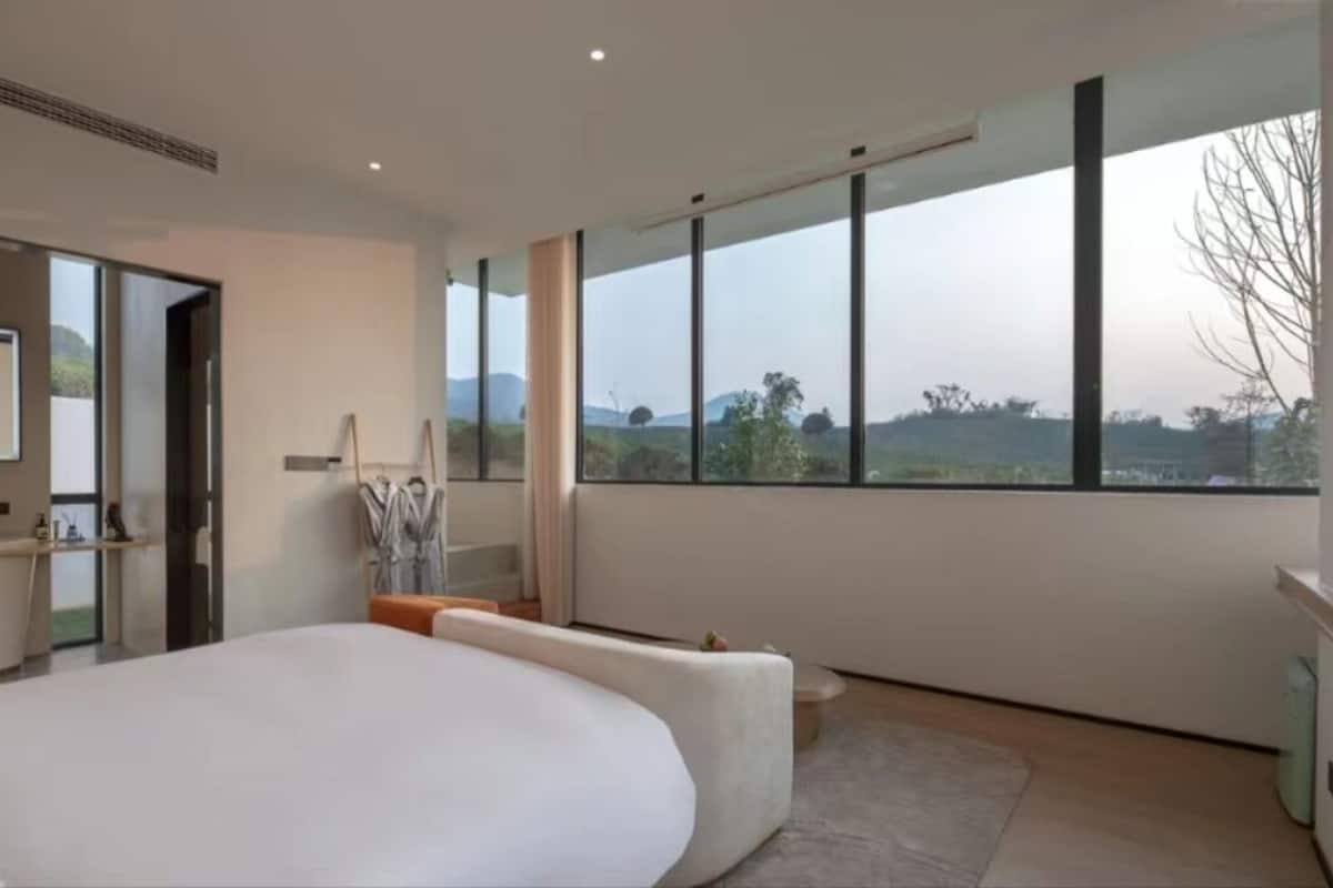A modern bedroom with a large bed, a view of the countryside through large windows, and a minimalist design.