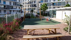 Un terrain de jeux avec un banc en bois, entouré d’une clôture blanche et de verdure.