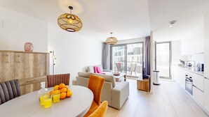 Un salon moderne comprenant un coin repas, un canapé, une table basse et une cuisine visible à travers une porte ouverte.