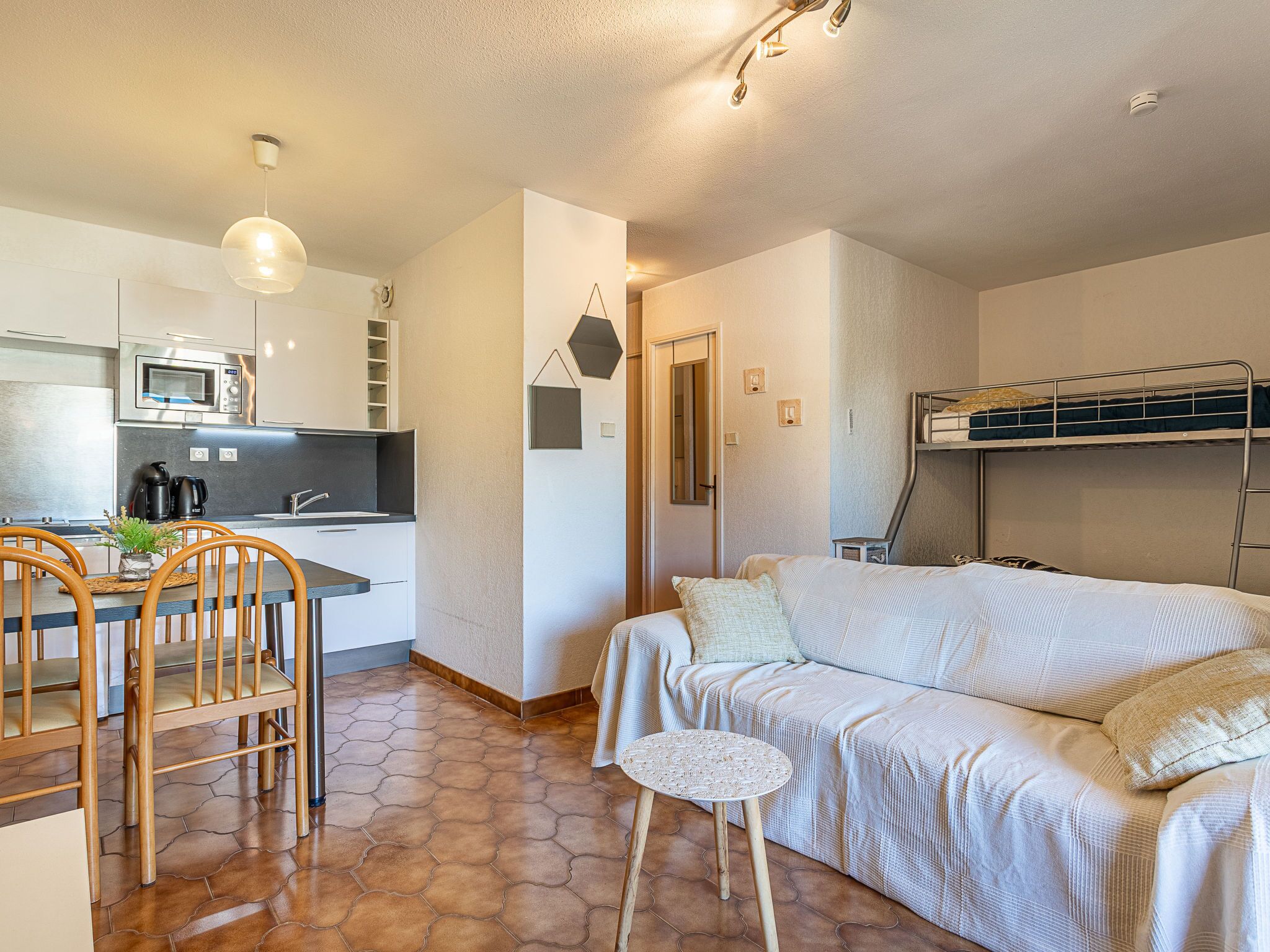 Kompakti hotellihuone, jossa on pieni keittiö, ruokailutila tuoleineen, sohva ja kerrossänky.