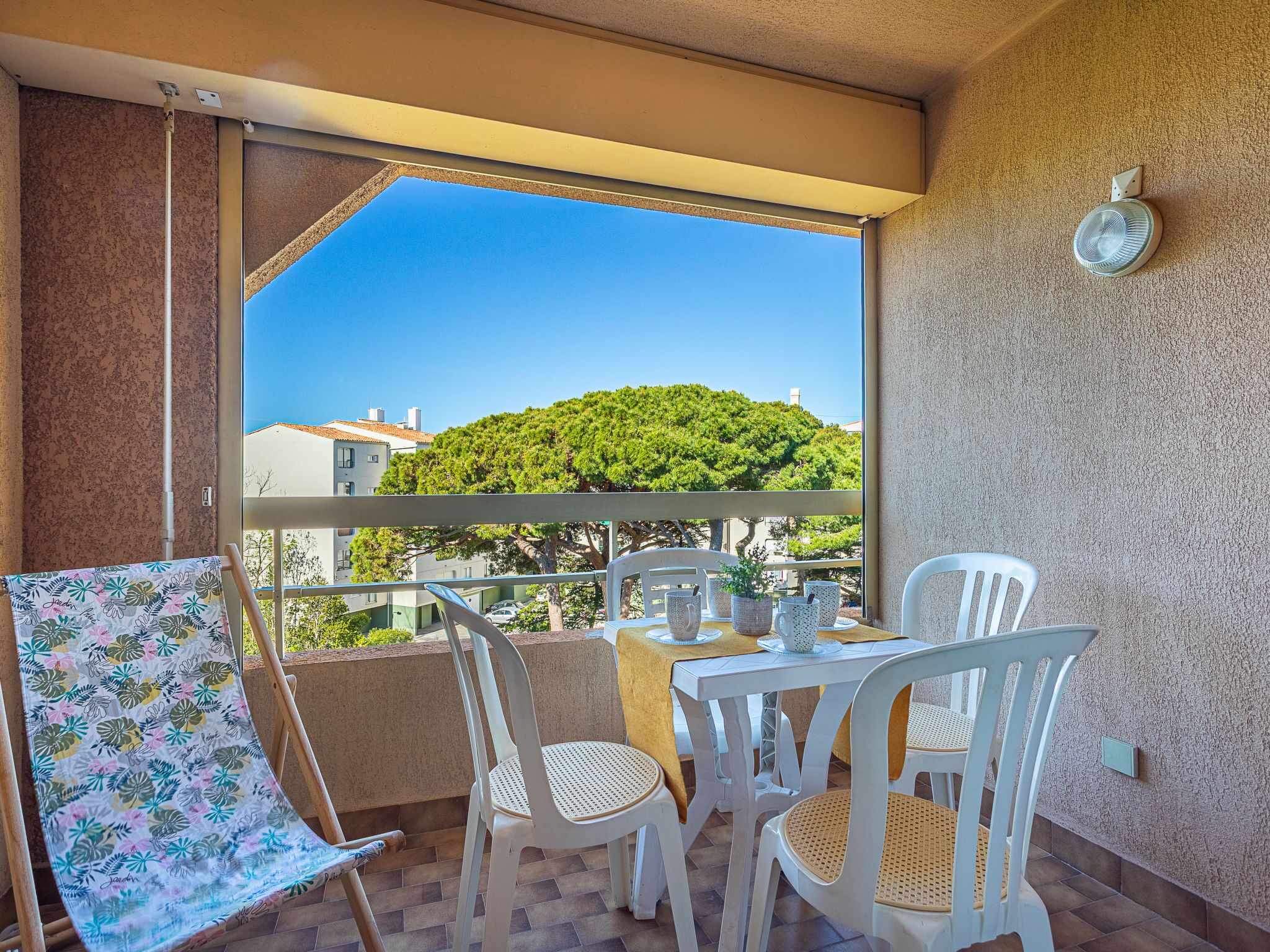 A balcony with a table and chairs, a view of a green hill, and a clear sky.