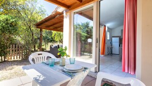 Eine Terrasse im Freien mit einem Tisch für zwei Personen, einer hölzernen Pergola darüber und Blick ins Haus durch eine Glastür.