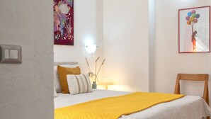 Ein Schlafzimmer mit einem Bett, einem Nachttisch, einer Lampe, einem Sessel und einer Wand mit einem Gemälde und einem gerahmten Bild.