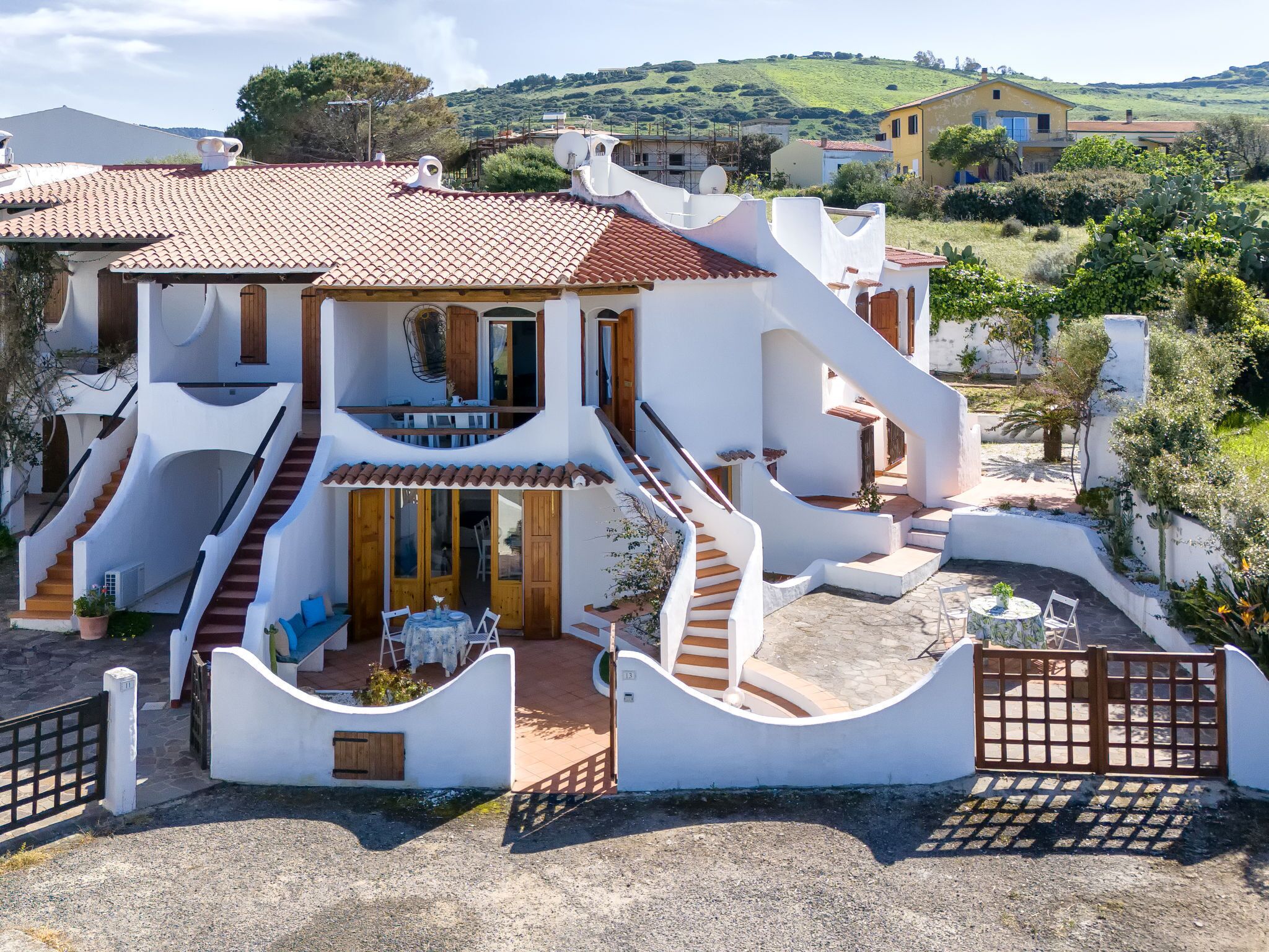 A white villa with a red-tiled roof, a central staircase, and a patio area with outdoor seating.