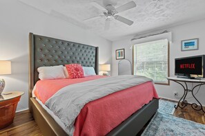 A modern bedroom with a tufted headboard, a bed with pink and white bedding, a ceiling fan, a television, and a window with blinds. - Hot Tub & Breathtaking View on Dale Hollow Lake (Albany)