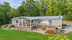 Ein zweistöckiges Haus mit überdachter Terrasse, Gartenmöbeln und einem Feuerkorb.
