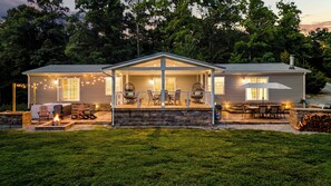 Ein zweigeschossiges Haus mit einer überdachten Terrasse, Sitzgelegenheiten im Freien und einer Feuerstelle.
