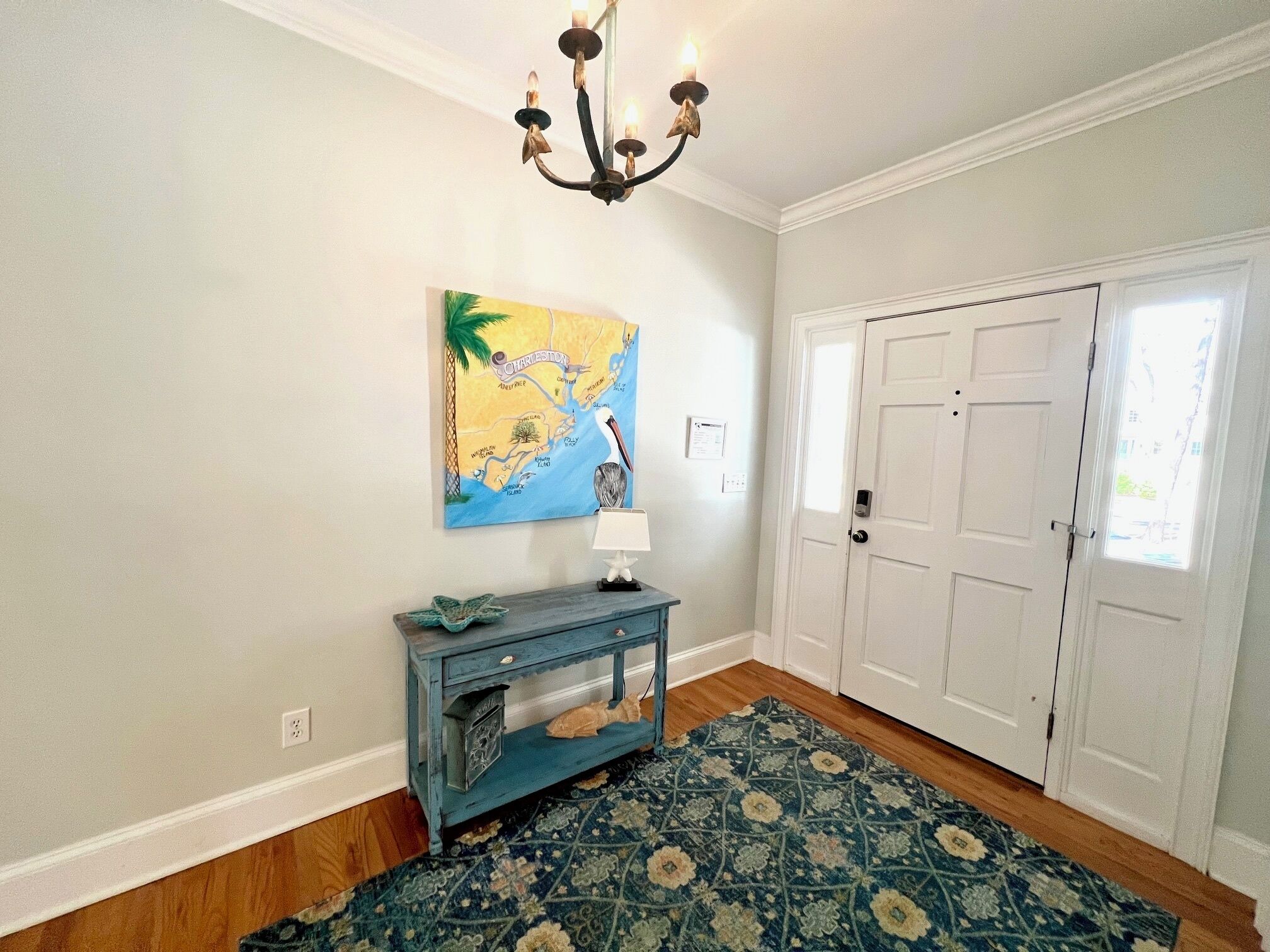 Un couloir avec une carte, une console bleue, un tapis à motifs et une porte blanche.