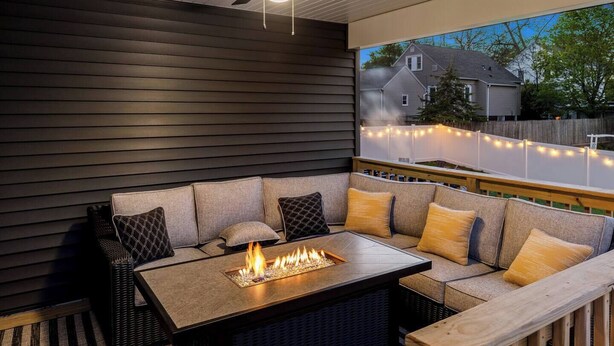 An outdoor seating area with a fire feature, dark siding, and a view of a neighboring house.