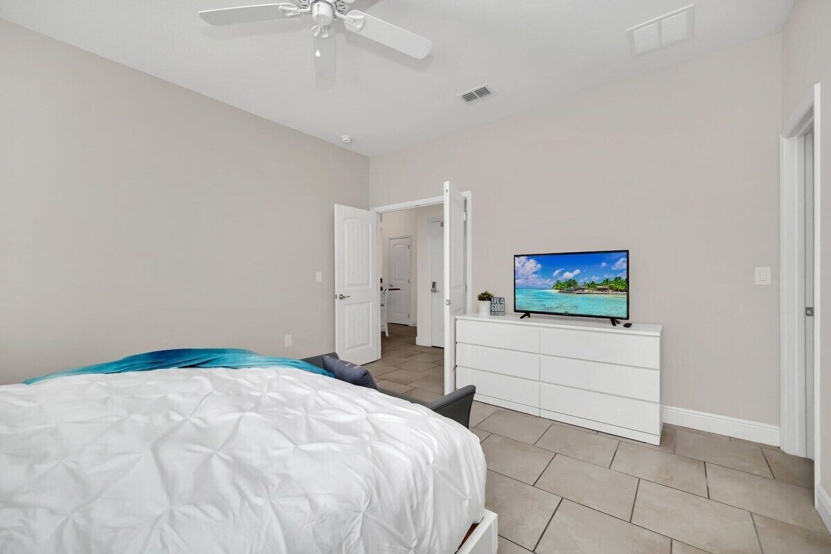A bedroom with a bed, a TV on a dresser, and a ceiling fan.