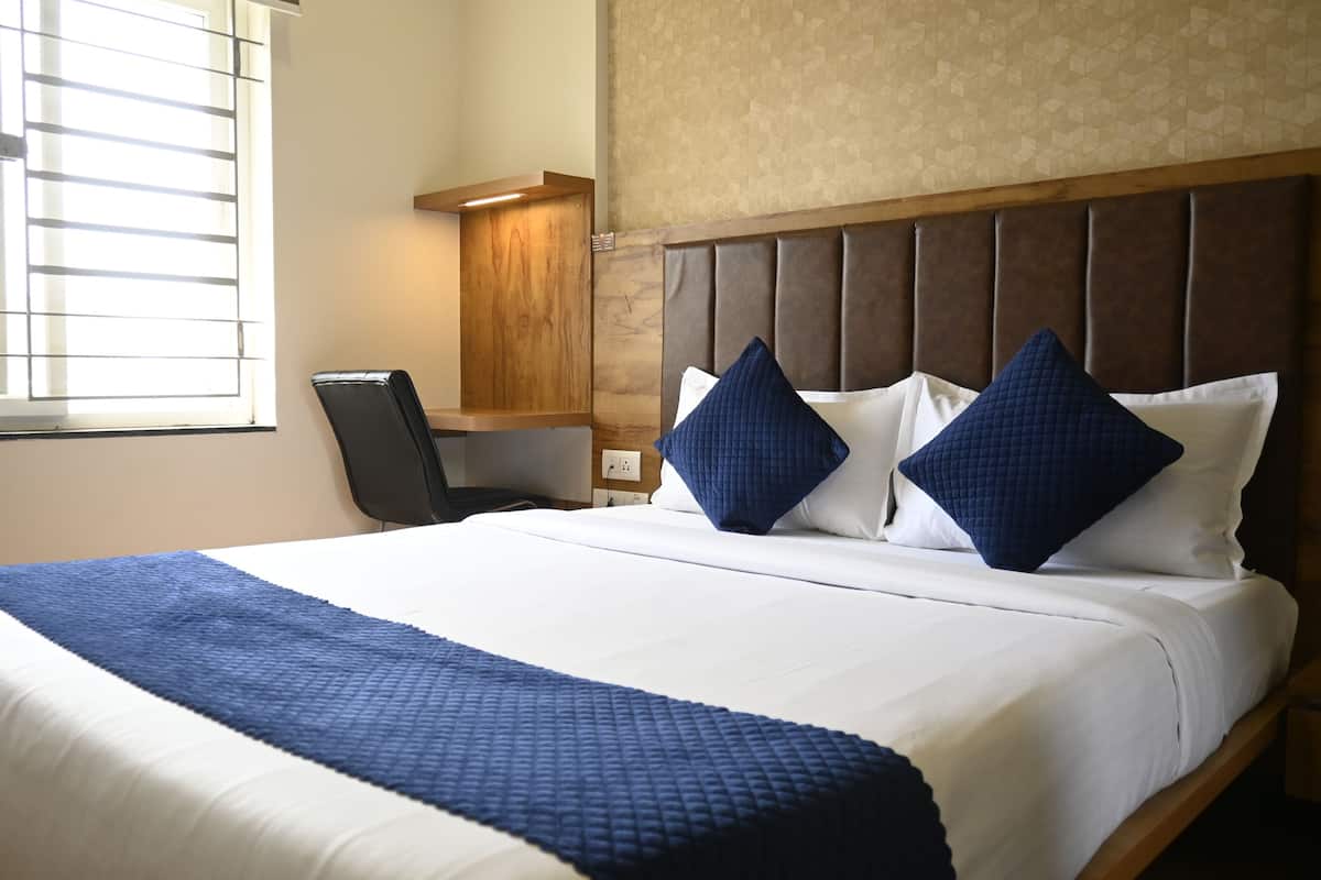 A hotel room with a large bed, a desk, and a window with blinds.