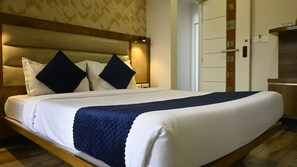 A hotel room with a large bed, a headboard, two dark pillows, a white bedspread, and a dark quilted blanket. - Hotel Rize Inn (Bengaluru)