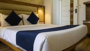 A hotel room with a bed, a nightstand, a wall-mounted lamp, and a door with a number. - Hotel Rize Inn (Bengaluru)