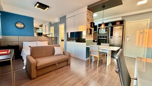 Ein modernes Wohnzimmer mit Sofa, Esstisch und Küchenzeile, inklusive Kühlschrank und Mikrowelle.