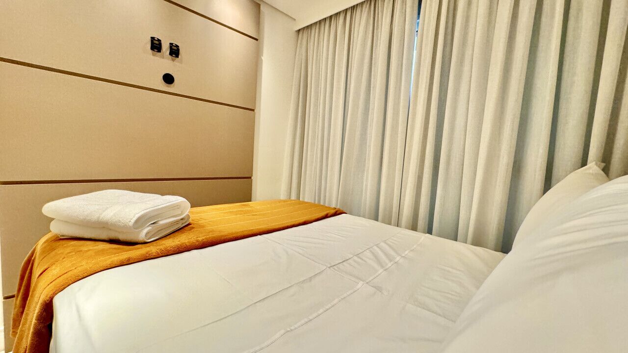 A hotel room with a neatly made bed, a wooden headboard, and a large window with curtains.