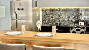 Una cucina moderna con frigorifero in acciaio inossidabile, zoccolo posteriore in mosaico di vetro e tavolo da pranzo in legno apparecchiato per due, con bicchieri da vino e piatti.