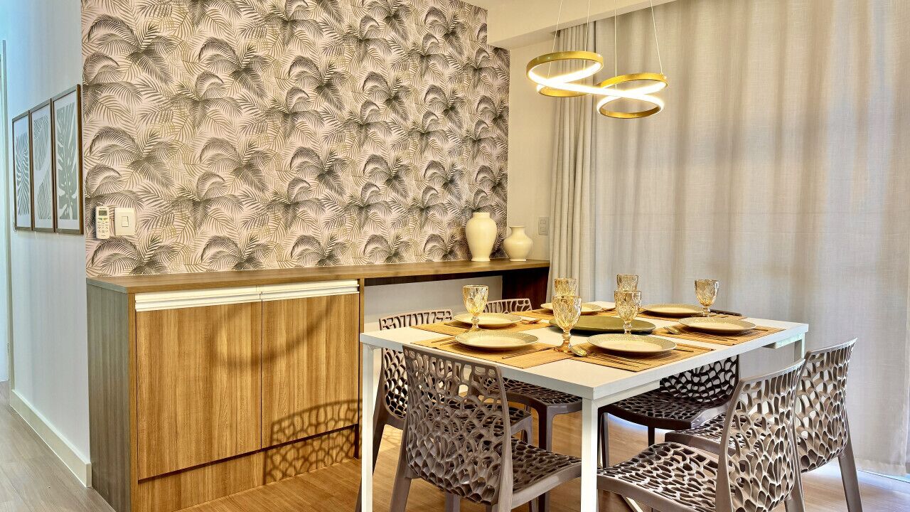 Un comedor con una mesa de madera dispuesta para cuatro, papel tapiz estampado e iluminación colgante moderna.