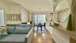Un salon moderne avec un canapé, une table à manger et des chaises. Un grand miroir orne le mur et offre une vue sur l’extérieur.