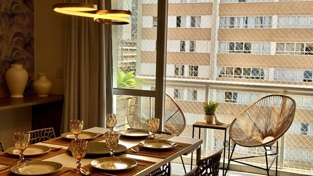 Un coin repas avec une table dressée pour quatre personnes, de grandes fenêtres et des chaises en osier.