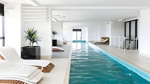 Ein modernes Hallenbad mit langem, schmalen Design, umgeben von weißen Wänden und einigen Blumentöpfen.