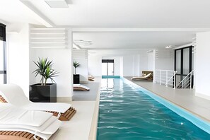 Une piscine intérieure moderne, de forme longue et étroite, entourée de murs blancs et agrémentée de quelques plantes en pot.