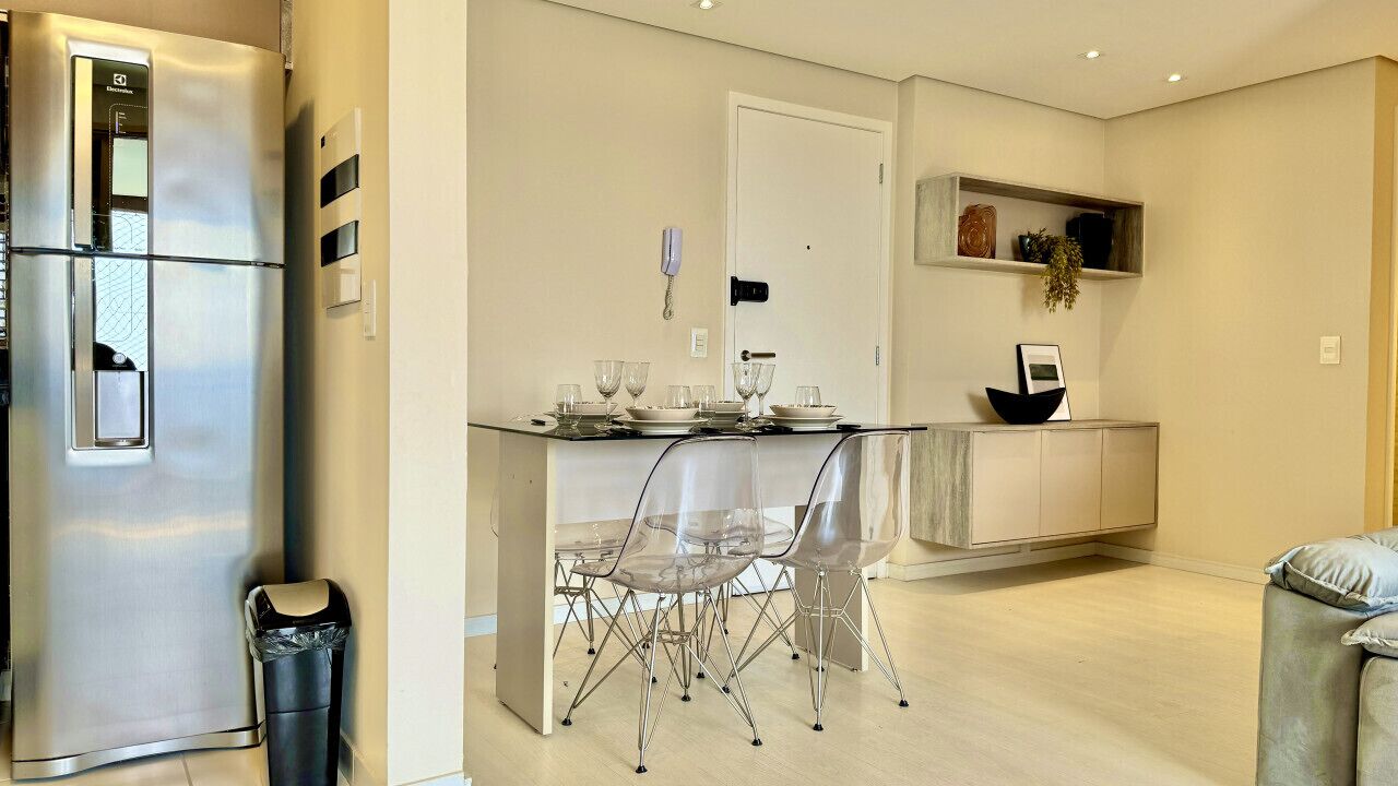 Un angolo cottura funzionale con frigorifero, una zona pranzo con sedie, un tavolino e un pensile con oggetti decorativi.