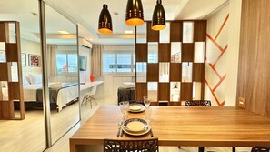 A modern hotel room with a wooden dining table set for two, a large mirror, and a decorative wall panel. - Incrível Studio com Lava Seca e vaga no Lifespace (Curitiba)