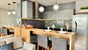 A modern kitchen with a central island, pendant lighting, and a stainless steel refrigerator. - Premium Studio Lifespace Curitiba Batel com vaga (Curitiba)
