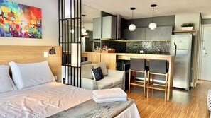 A modern hotel room with a bed, a sofa, a small kitchen area, and a dining table. - Premium Studio Lifespace Curitiba Batel com vaga (Curitiba)