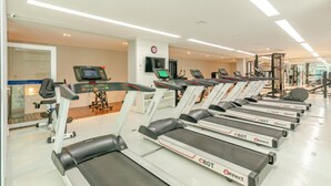 Un gimnasio con cintas de correr, equipo de ejercicio y una pantalla digital.