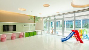 A spacious indoor play area with a large window, a television, and colorful play equipment.
