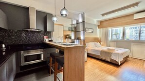 A modern hotel room with a kitchen area, a bed, and a view of the city. - Luxo e Estilo juntos nesse Studio no Lifespace CWB (Curitiba)