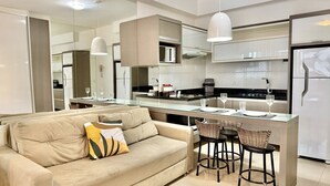 A modern kitchen with a central island, a sofa with cushions, and a dining area with bar stools. - Studio Top em frente ao Shopping Curitiba, Batel (Curitiba)