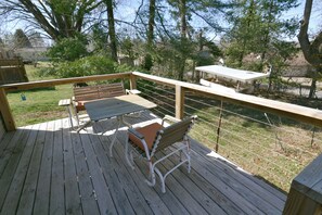 A wooden deck with a table and two chairs, surrounded by a wooden railing and trees. - The Boho Roost (Bloomington)