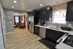 A modern kitchen with dark cabinets, stainless steel appliances, and a large window with curtains. - The Boho Roost (Bloomington)