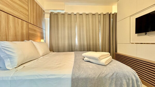 A hotel room with a bed, a TV mounted on the wall, and a window with curtains.