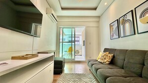 A modern living room with a sofa, a coffee table, and a TV. There is a sliding glass door leading to a balcony. - 1 Quarto, Sacada e Churrasqueira Lifespace Batel (Curitiba)